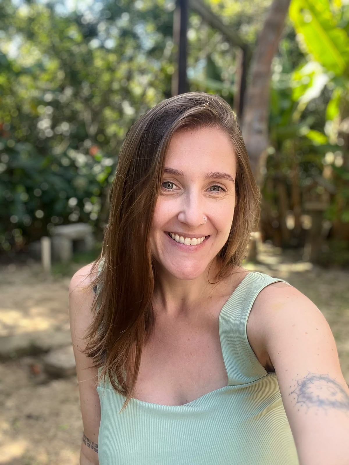 Ana Carolina Biondo, psicóloga, sorrindo em uma área externa com plantas ao fundo